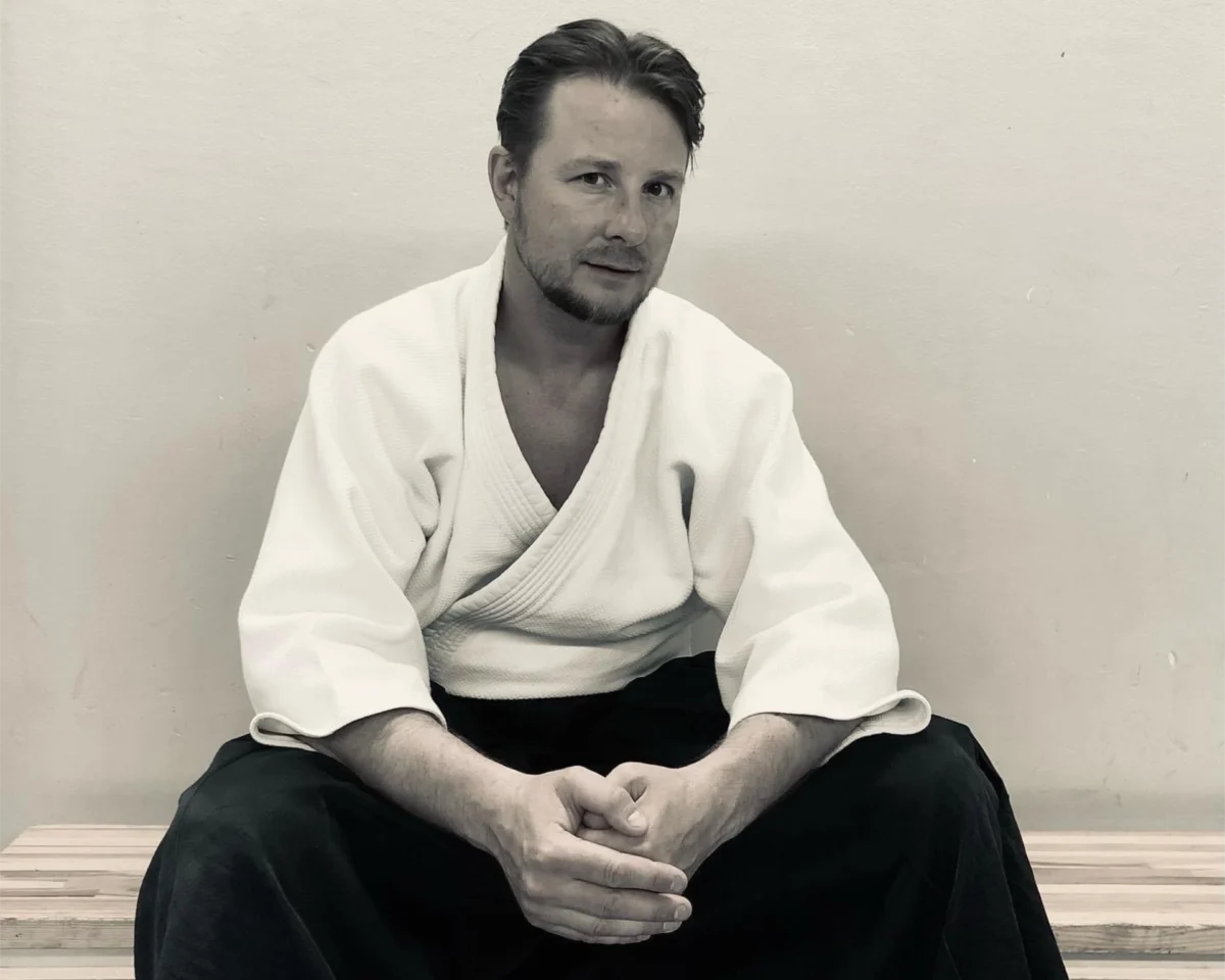 Black and white portrait of David Gramnaes sitting on a bench and wearing clothes for martial arts practice.